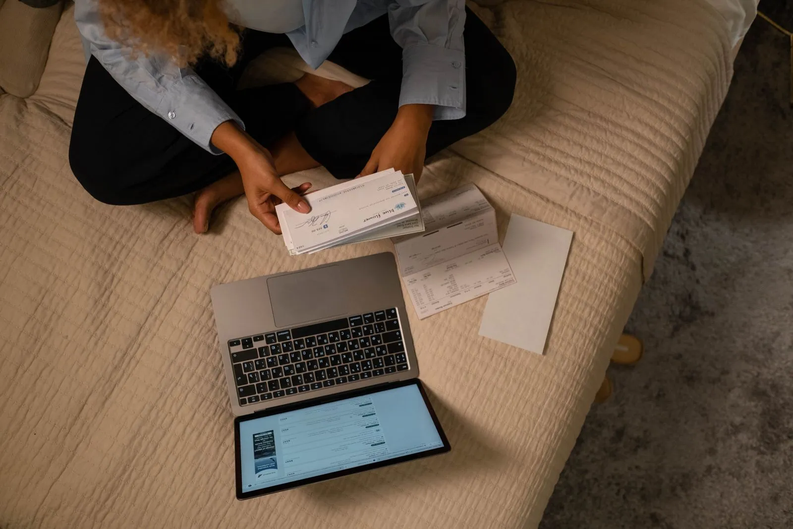 Person reviewing paper checks and paperwork next to a laptop