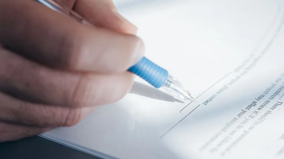 Close-up of a hand signing a paper document with a pen